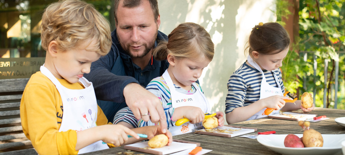 Kinder und Erzieher schneiden gemeinsam Gemüse an einem Tisch
